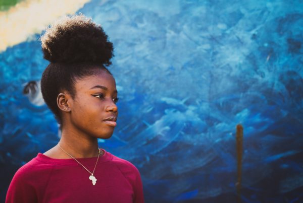 young black woman looks into the distance against a blue painted background