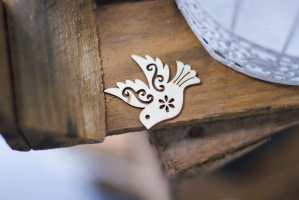 ornate wood cut-out of a dove lays on top of rough wooden table