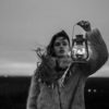 black and white photo of young woman in fur coat holding a lantern