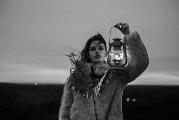 black and white photo of young woman in fur coat holding a lantern