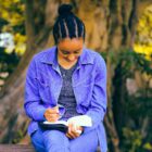 young Black woman reads Bible on an outside bench