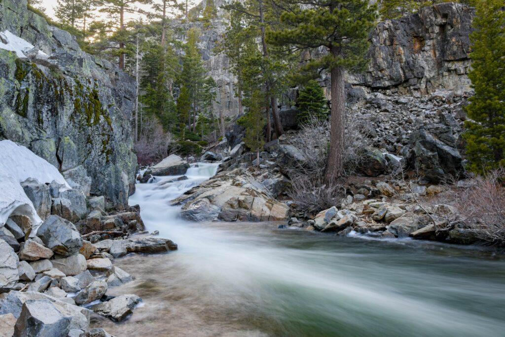 time lapse photo of flowing stream in between big rocks and trees