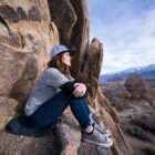 young woman sits on rocks looking thoughtfully out into mountains