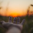 selective focus image of outreached hand in front of sunset