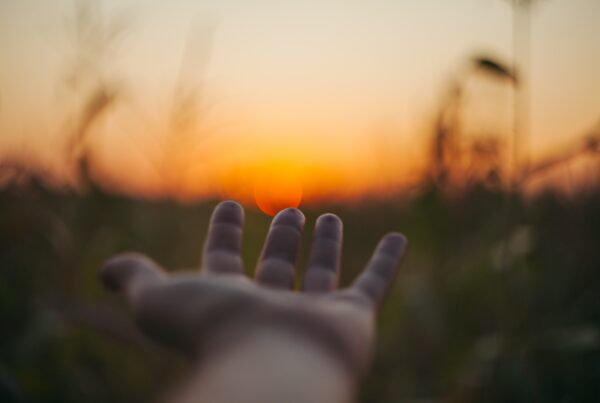 selective focus image of outreached hand in front of sunset