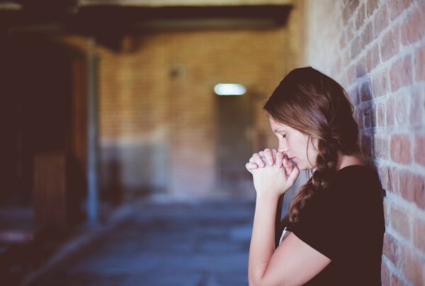 young woman prays in small brick room