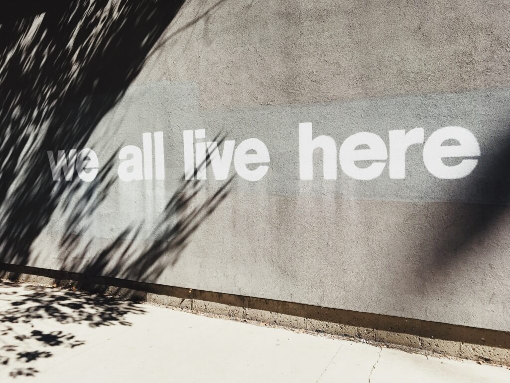 muro de cemento gris con las palabras "todos vivimos aquí" pintadas con spray en blanco
