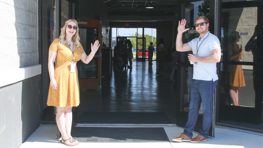 man and woman smile and wave at open church doors