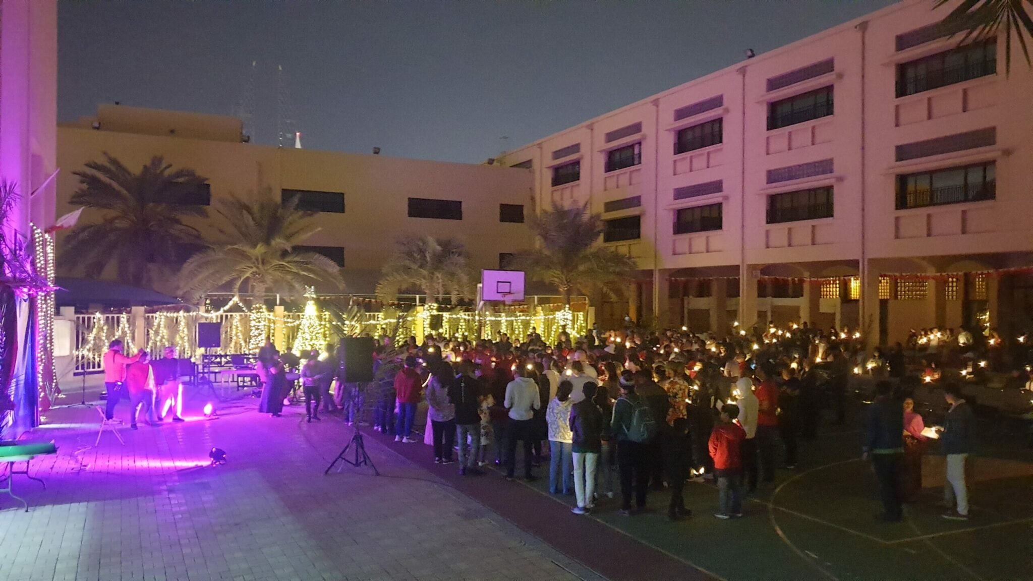large group of people sing Christmas carols by candlelight in outside courtyard
