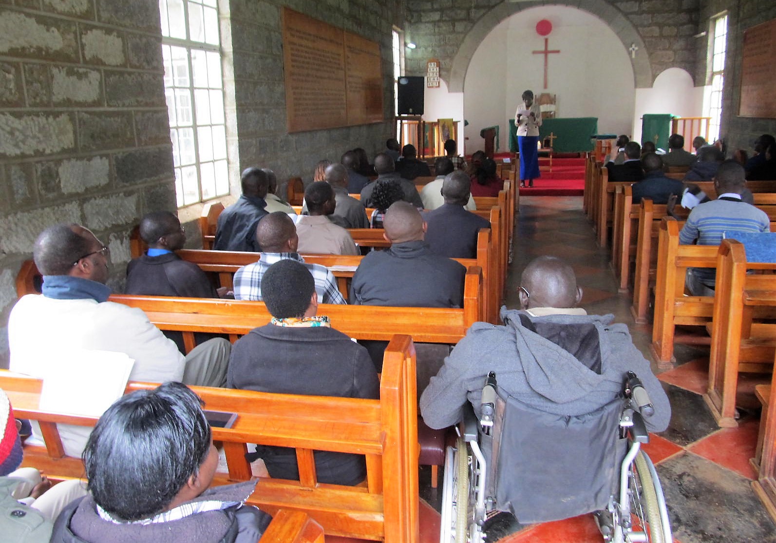 Personas sentadas en bancos de madera durante la capilla de Navidad en la Universidad St Pauls de Kenia.
