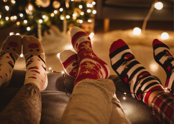 three pairs of feet in Christmas socks lined up in front of Christmas tree