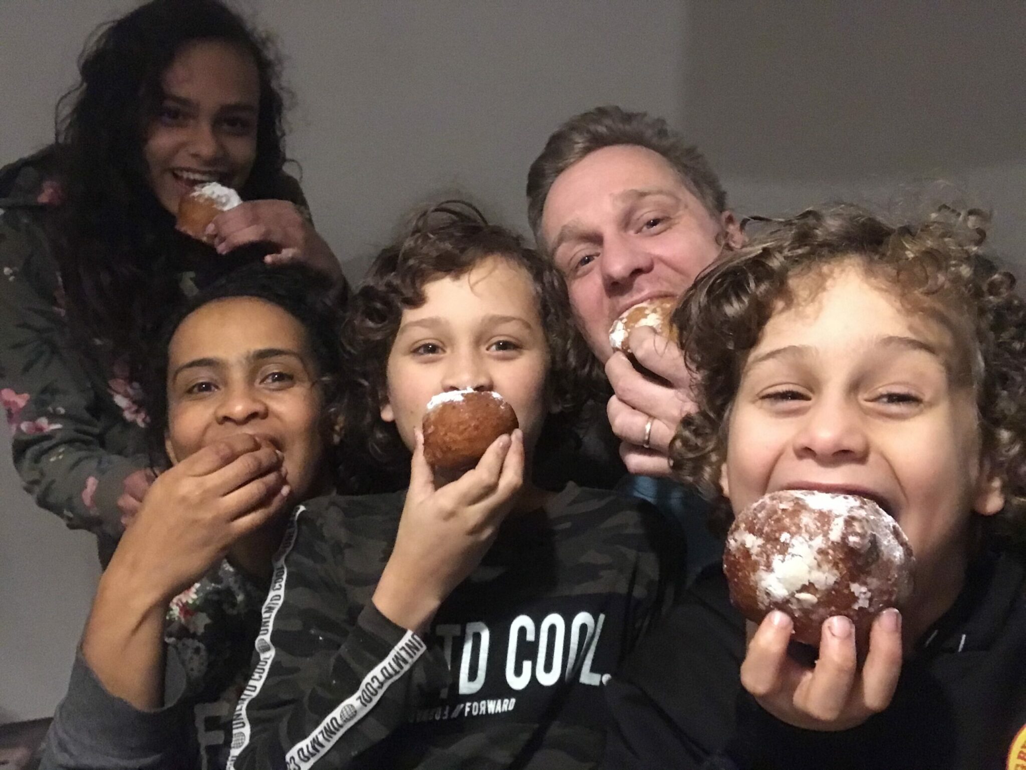 family of five eats oliebollen (fried dough with raisins and powdered sugar) with big grins