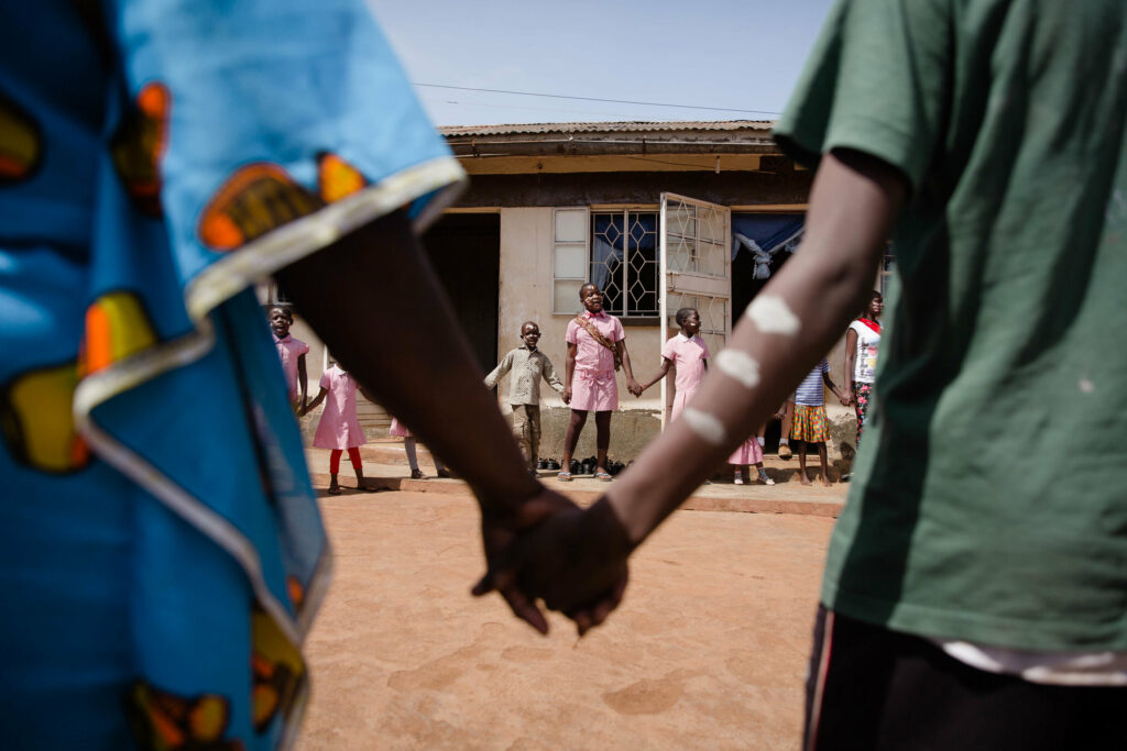 close up of two African hands holding one another with circle of kids in background
