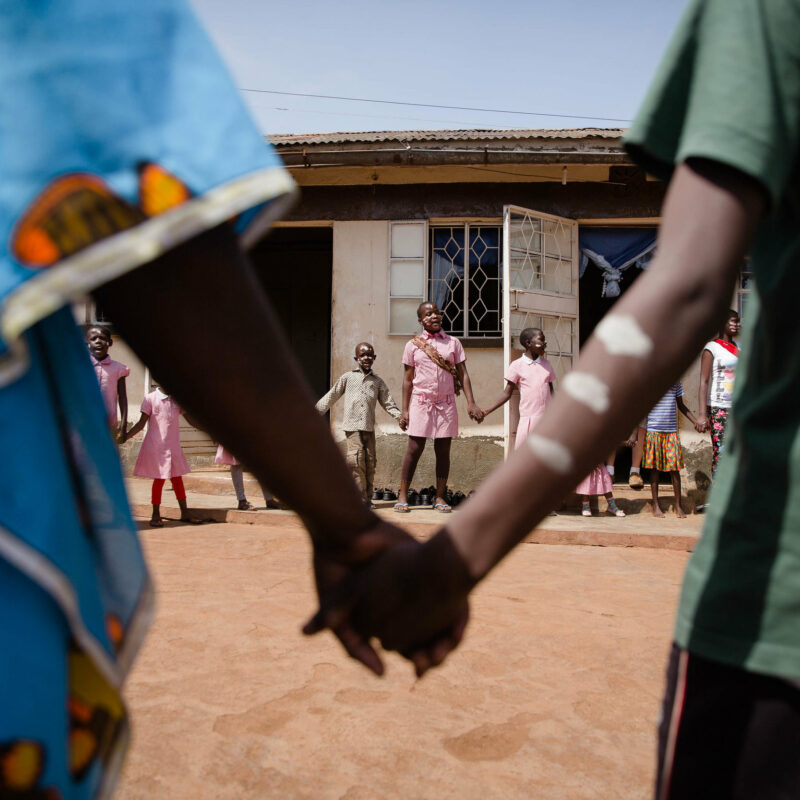 close up of two African hands holding one another with circle of kids in background