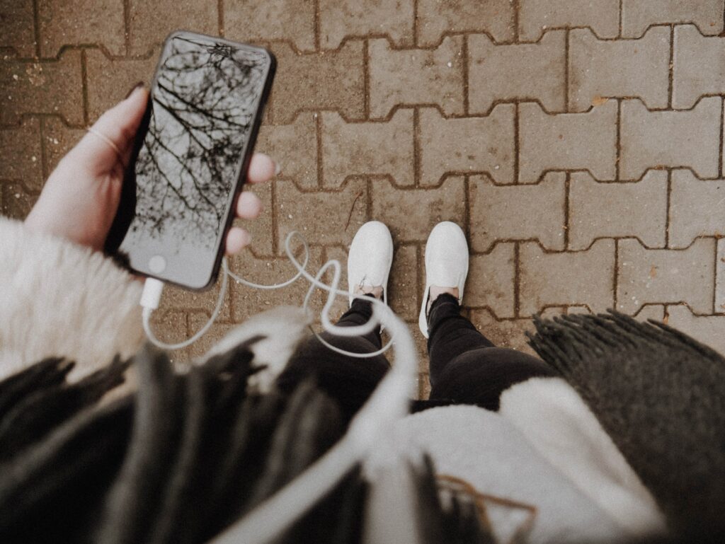 feet on brick pathway with phone and earbuds in hand