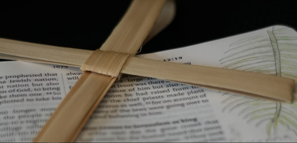 una cruz hecha con ramas de palmera secas sobre una Biblia abierta con un dibujo de una rama de palmera en los márgenes